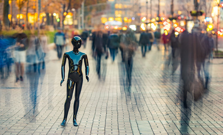 A black robot stands still on a crowded city street as pedestrians pass by.
