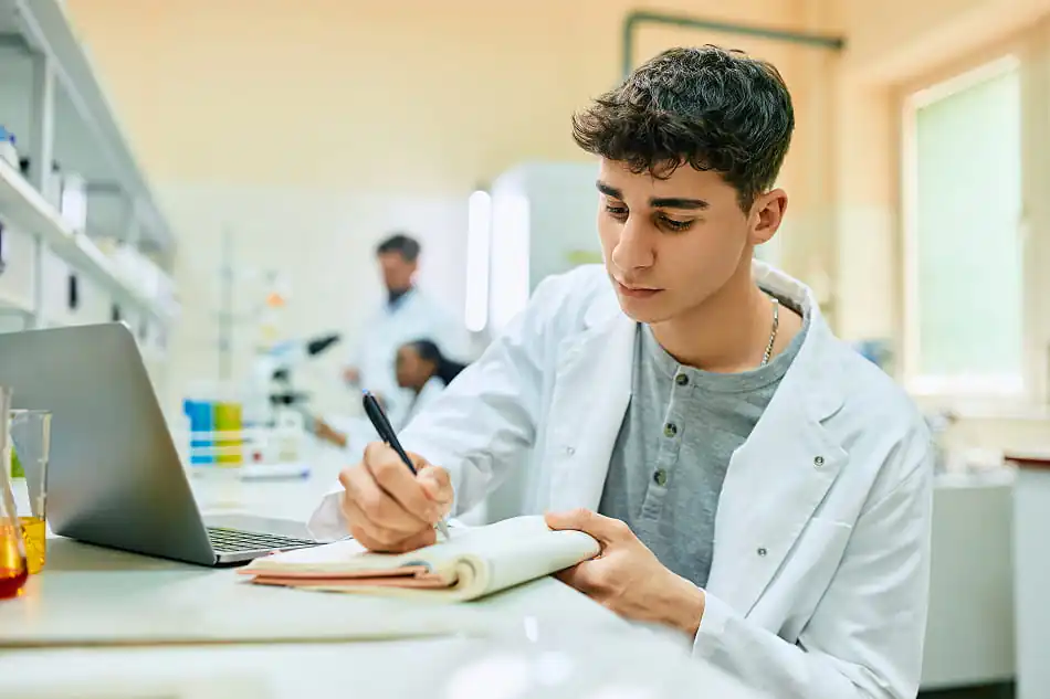 A young researcher in a science lab writing in a journal.