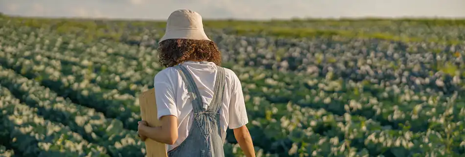 High school student walking through a crop field with a clipboard.