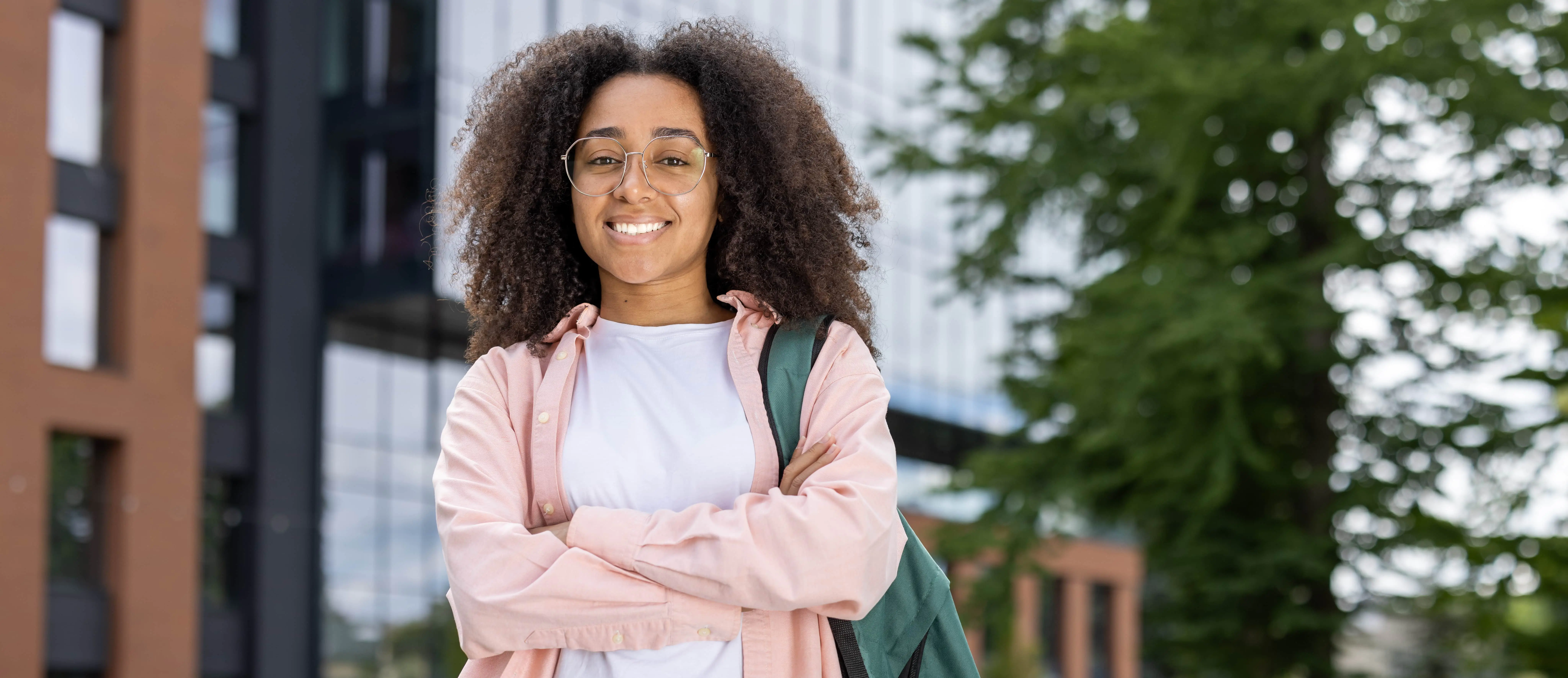 Teen female student posing confidently with backpack in front of a school